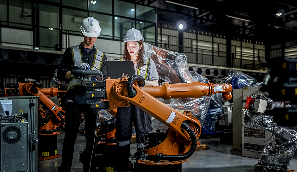 Two people standing over a welding machine with a remote system in an industrial factory