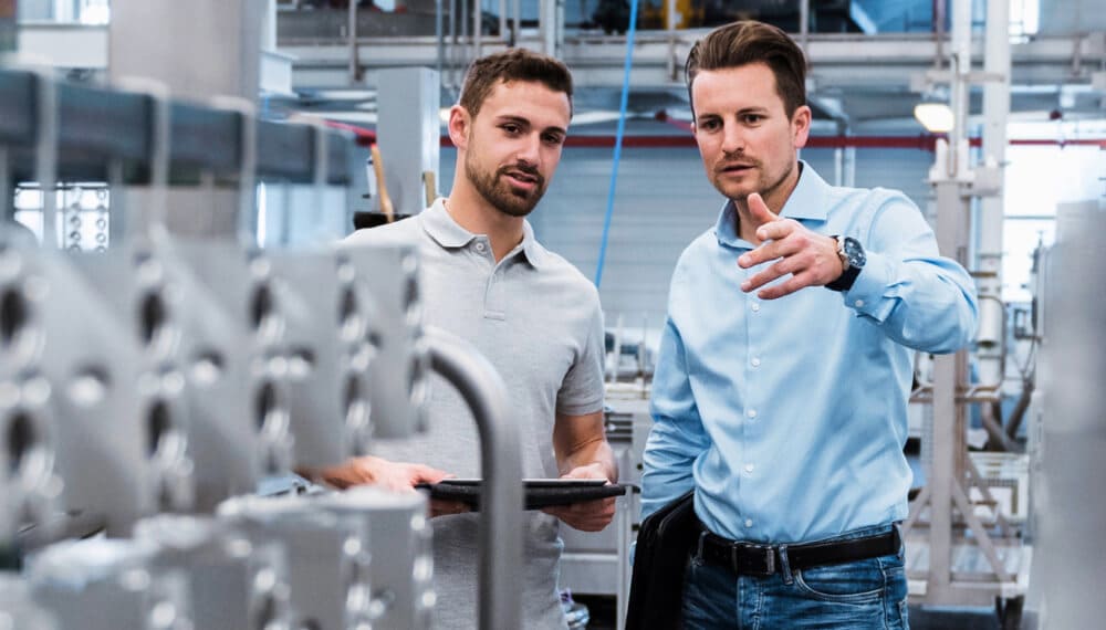 Business man showing his employee holding a tablet ERP manufacturing parts inside a factory