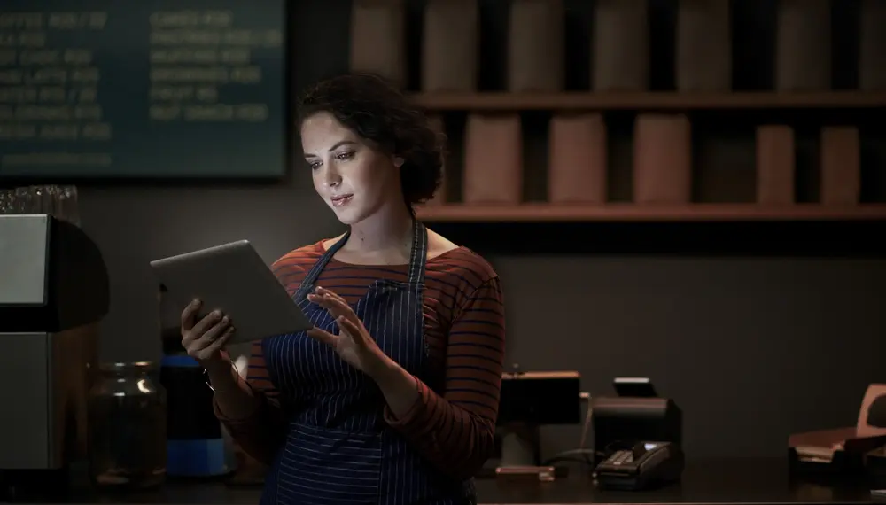 A cafe owner dressed in an apron inspects inventory stock on a tablet
