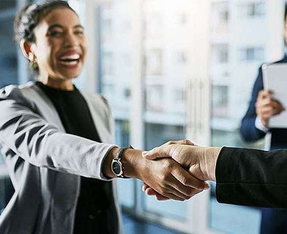 A smiling woman shakes hands with a business prospect.